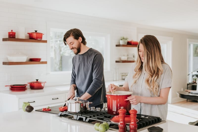 man and woman preparing meal while standing in the kitchen
