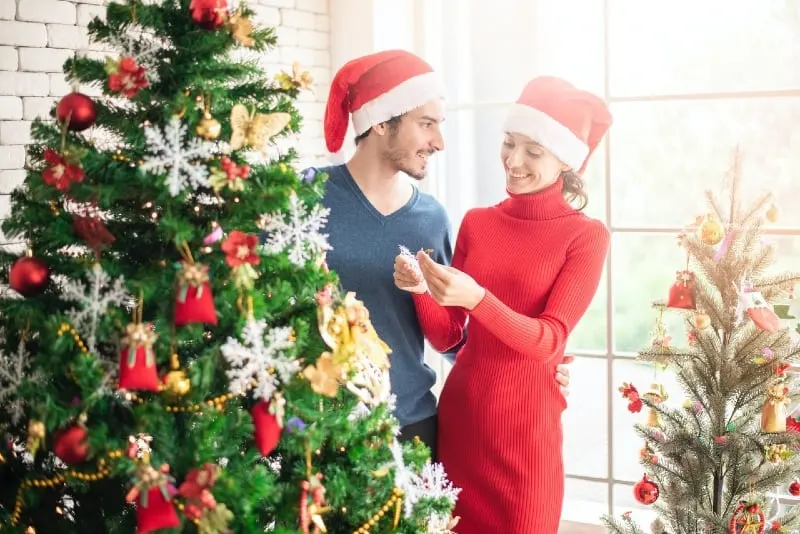 man and woman with red hats standing near christmas tree