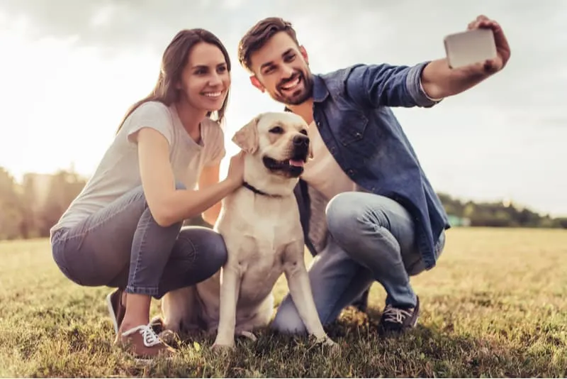 couple taking selfies with a dog squatting outdoors