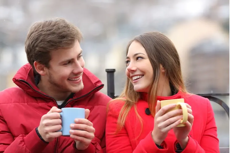 couple talking relaxed sitting on bench outdoors sipping coffee