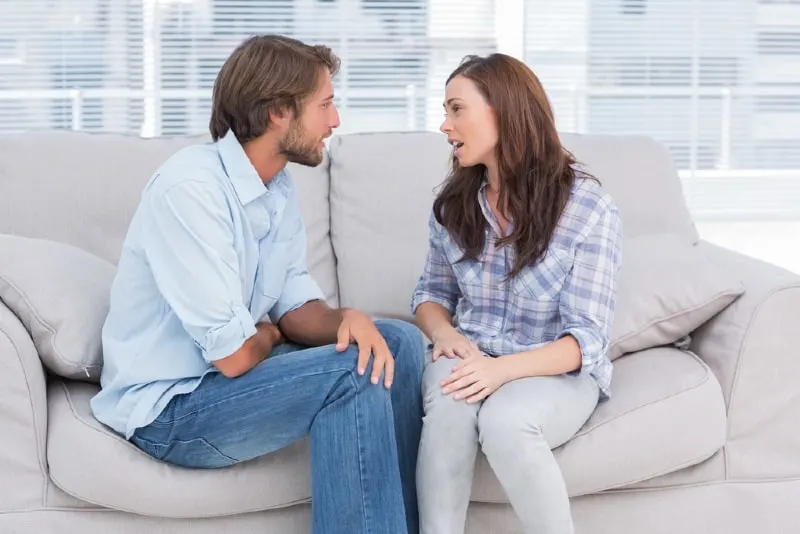man and woman talking while sitting on sofa