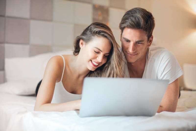 man and woman using laptop while lying on bed