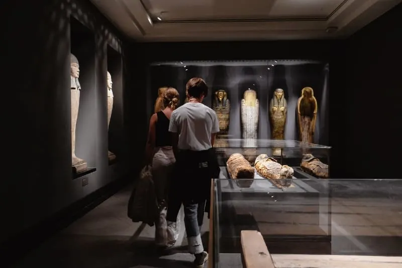 man and woman walking near mummies in museum