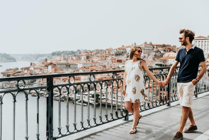 uomo e donna che si tengono per mano mentre camminano su un ponte