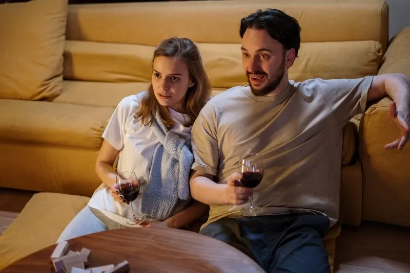 man and woman watching movie while holding glasses of wine