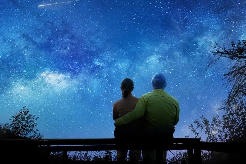 couple waching the stars during nightime sitting on a bench outdoors
