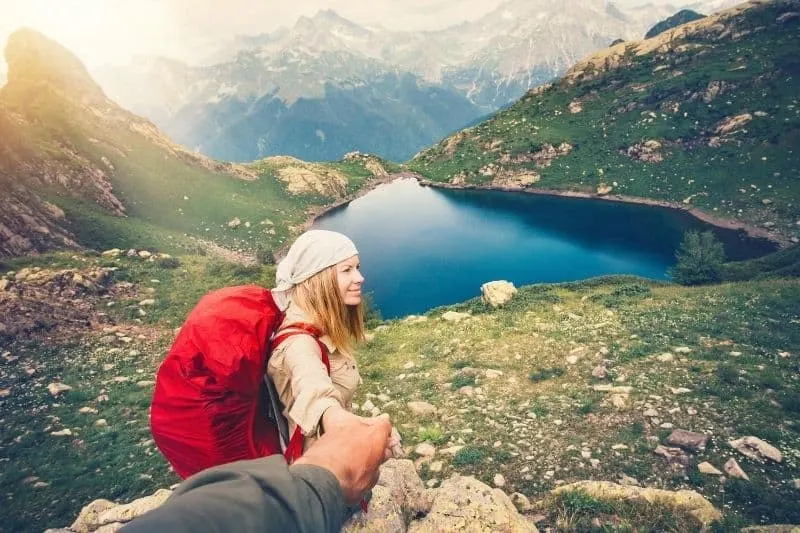 couple woman holding hand with a man travelling near the mountain and a body of water
