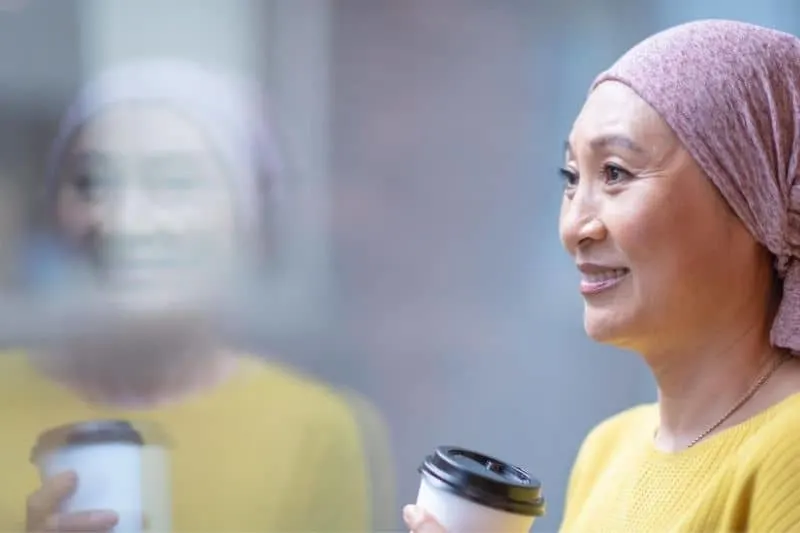 courageous korean woman having cancer holding a cup of coffee standing near a glass wall
