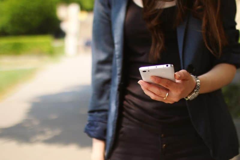crop image of a woman holding a white smartphone outdoors