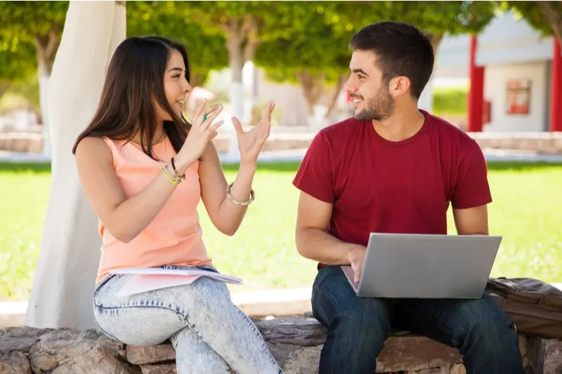 cute woman talking with man doing something on laptop sitting on the bench outdoors