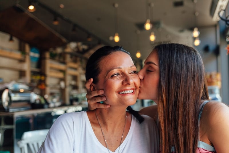 daughter kissing mother while sitting in cafe
