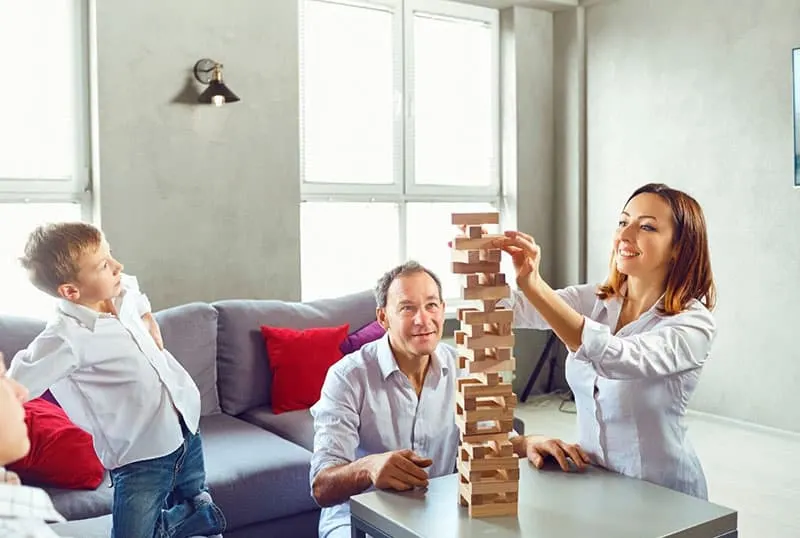 family playing jenga block inside living room with womans turn to play