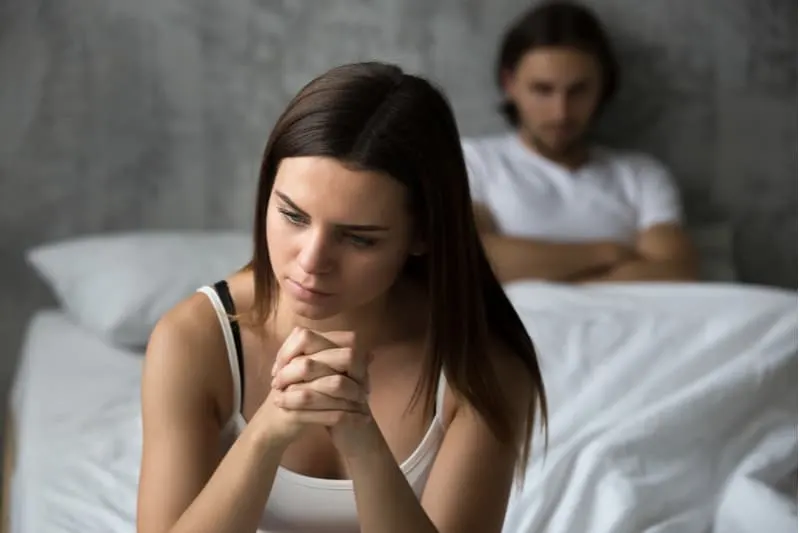 frustrated sad girlfriend sitting in bed with boyfriend at her back