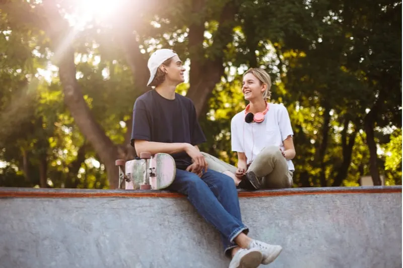 guy with a skateboard sitting next to a woman with headphones