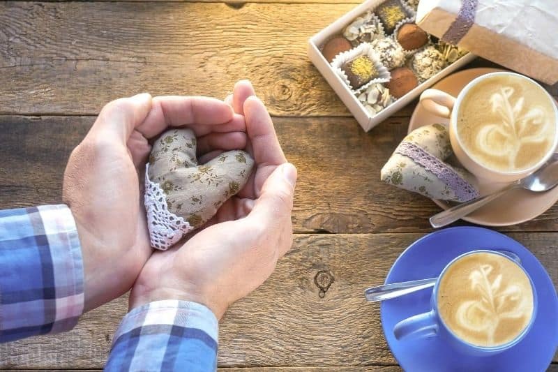 corazón hecho a mano en la mano de un hombre con bombones y café durante una cita de san valentín