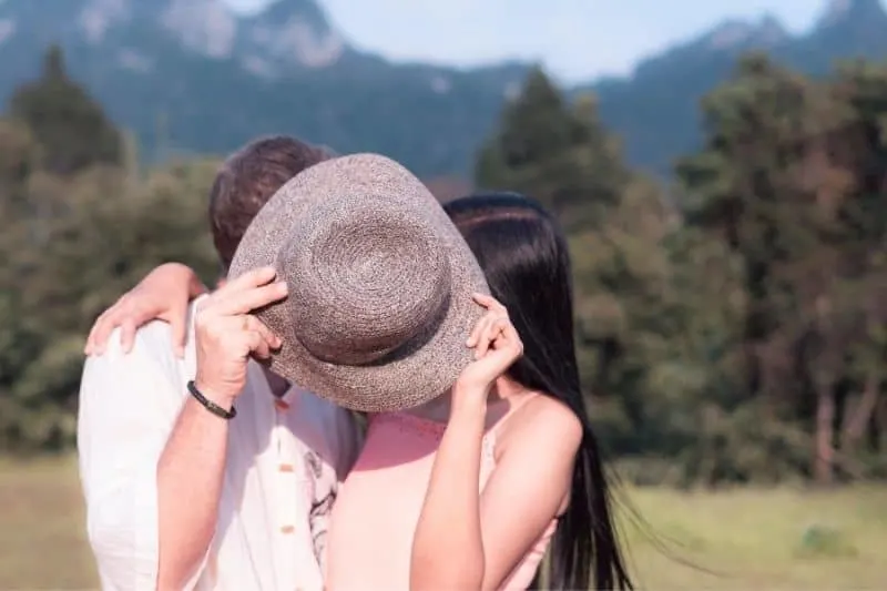 happy couple kissing outdoors covering their face with a hat