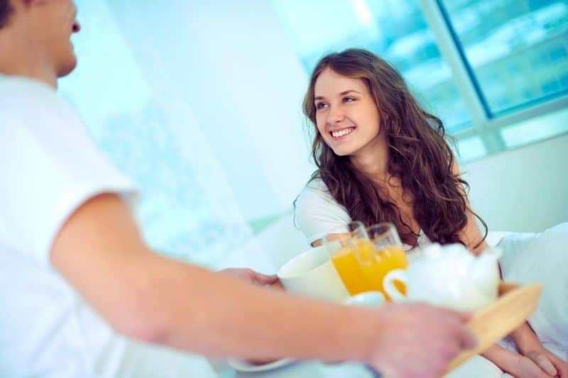 mujer feliz mirando a su marido trayendo el desayuno a la cama