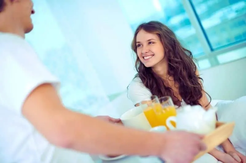 happy female looking at her husband bringing breakfast in bed