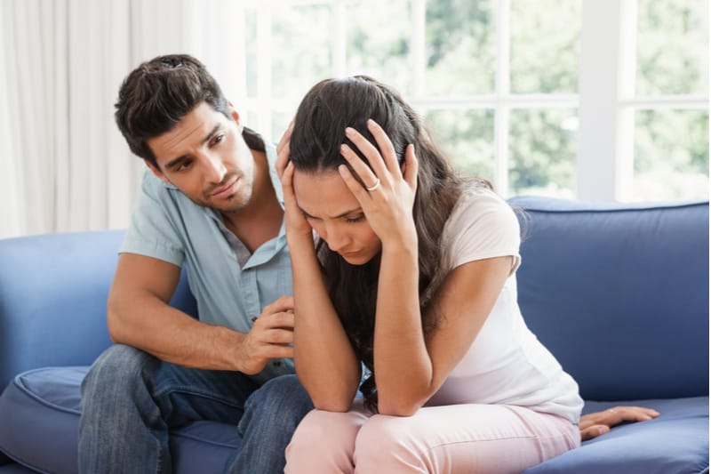 marido consolando esposa del dolor sentado en un sofá azul dentro de la sala de estar