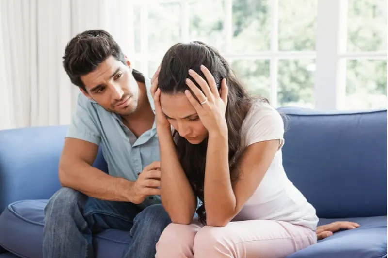 husband comforting wife from pain sitting on a blue couch inside living room