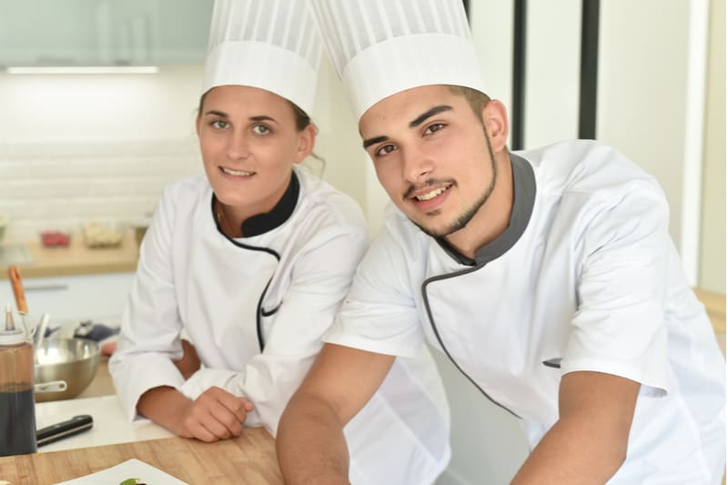 hombre y mujer asistiendo a una clase de cocina con uniforme de chef
