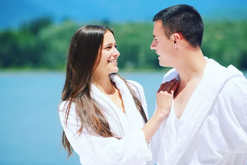 man and woman in white robe standing near the body of water