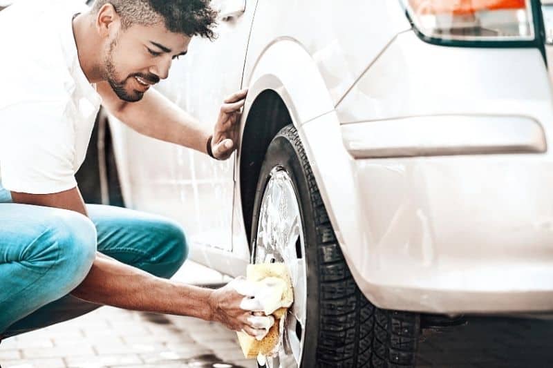 hombre limpiando las ruedas del coche con esponja y jabón