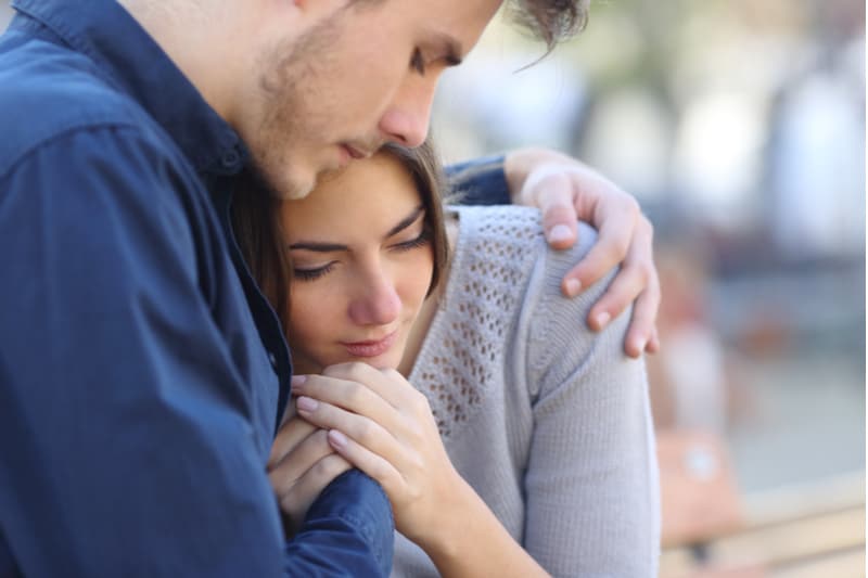 man comforting woman who's in pain by putting his arms around her