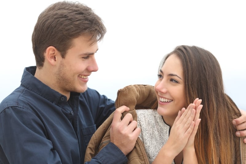 hombre sonriente dando chaqueta marron a mujer