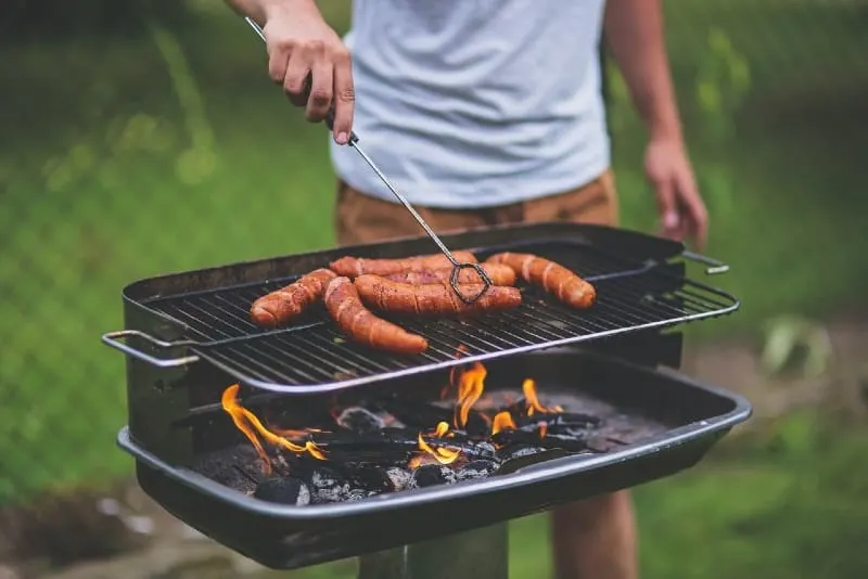 man in white shirt grilling sausages