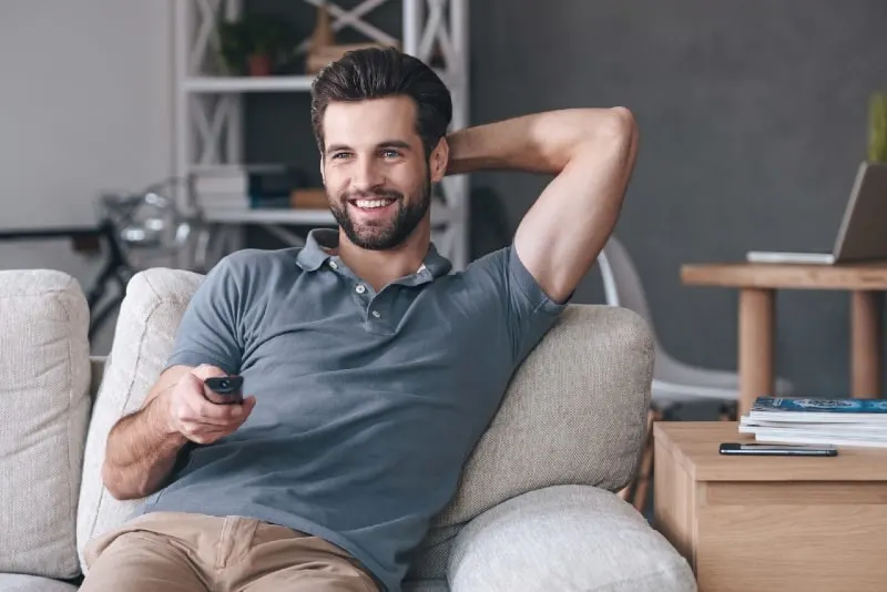smiling man holding remote control while sitting on sofa