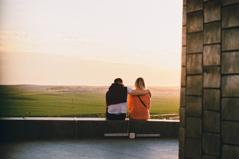 man hugging woman while sitting on concrete bench