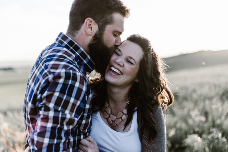 man kissing woman while standing in grass field