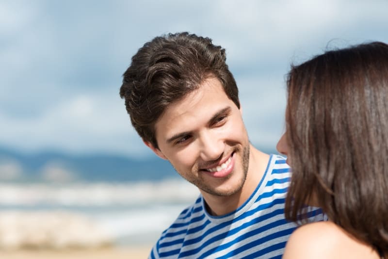 homem sorridente a olhar para uma mulher sentada na praia