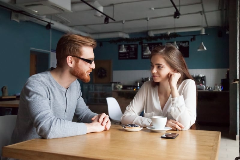 man with eyeglasses looking at woman while sitting at table