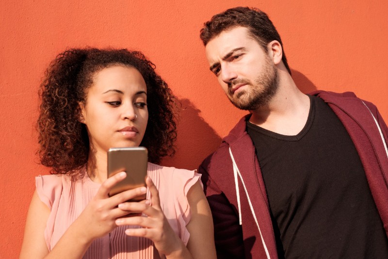 man looking at woman's phone while standing near orange wall
