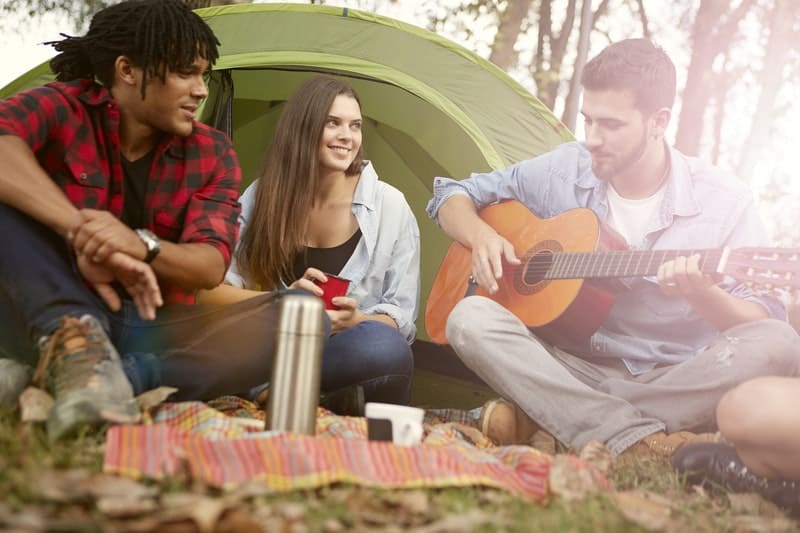 uomo che suona la chitarra durante un campeggio con gli amici che ascoltano 