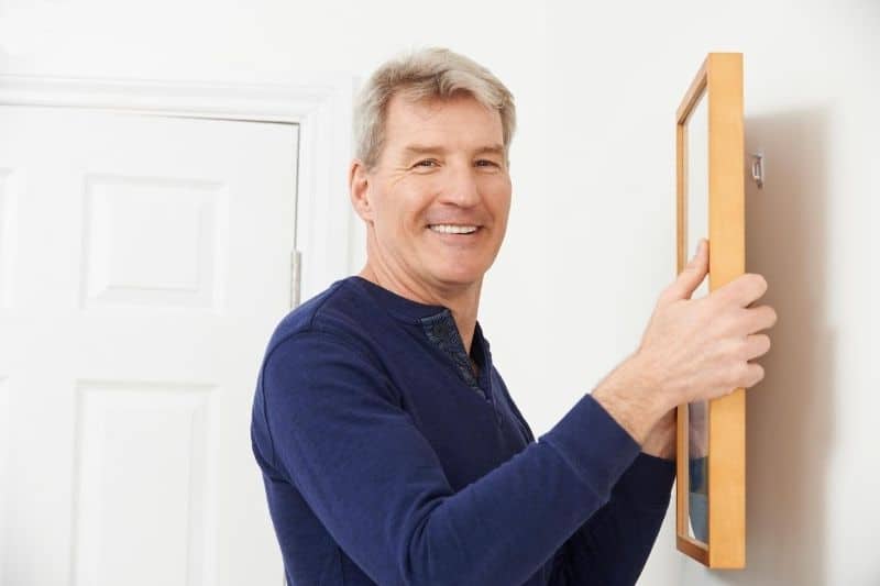 man putting picture frame on the white wall