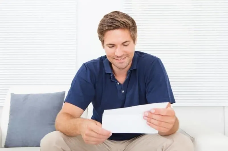 man reading a letter smiling and sitting in the couch smiling