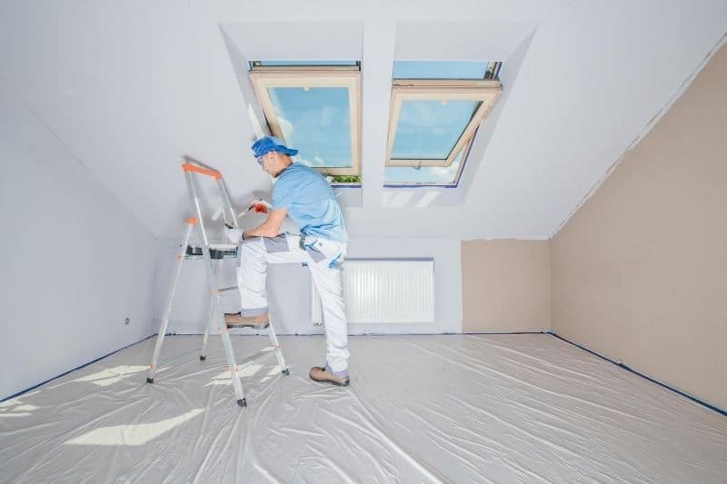 hombre pintando una habitación en el ático con ventanas en el techo