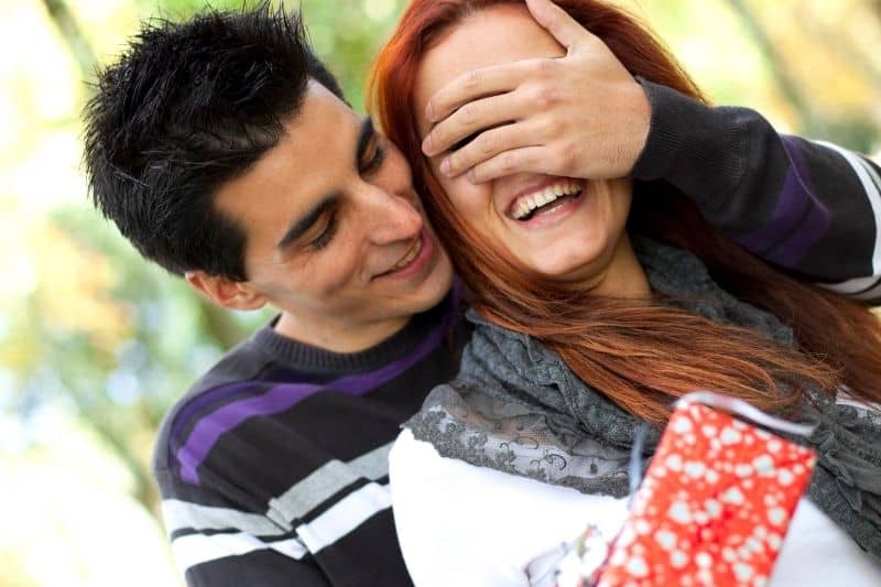 hombre sorprendiendo a su novia con un regalo tapándole los ojos