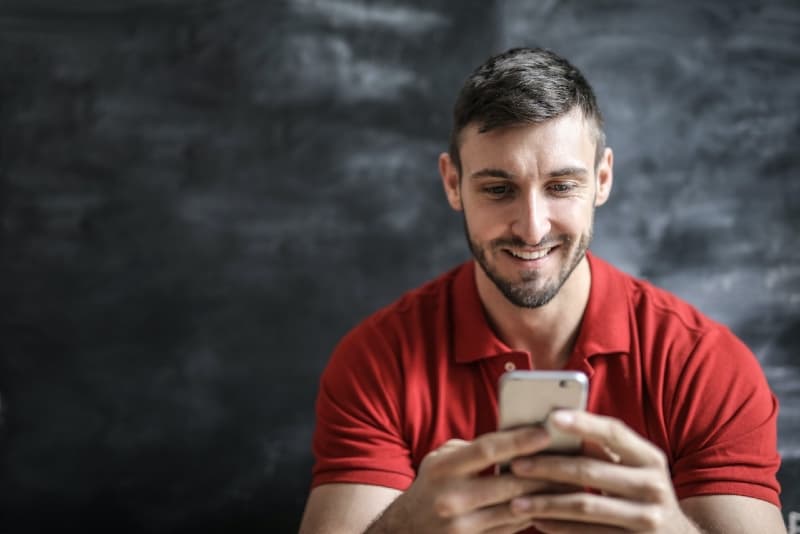 hombre sonriente con camiseta roja usando un smartphone