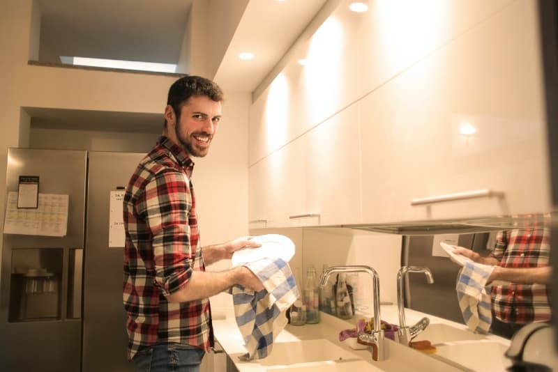 homem sorridente a lavar pratos na cozinha