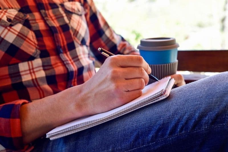 man writing poem on the notebook with coffee beside him