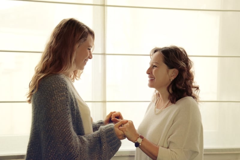smiling mother in white sweater and daughter holding hands