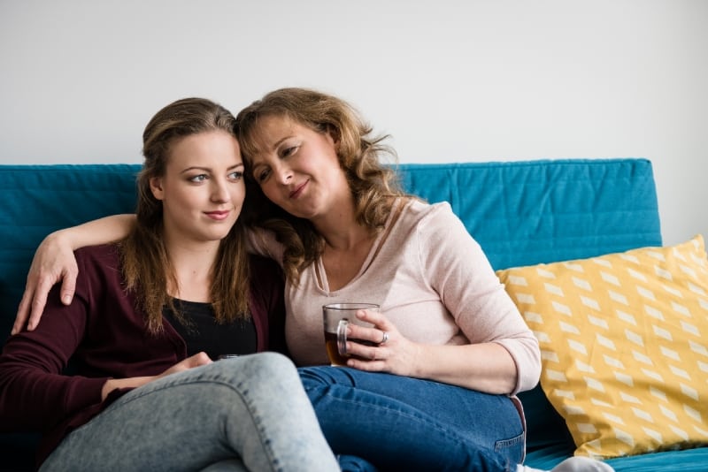 mother hugging daughter while sitting on sofa