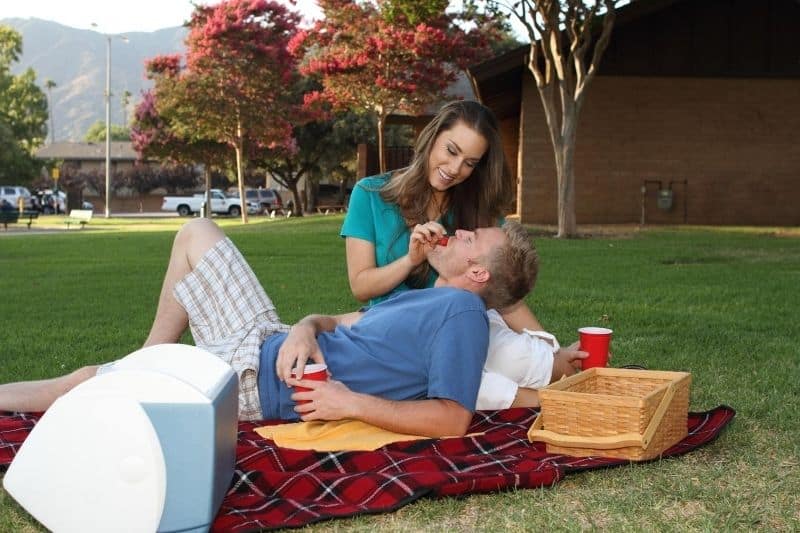 parque pareja picnic comiendo frutas y hombre tumbado en la colchoneta