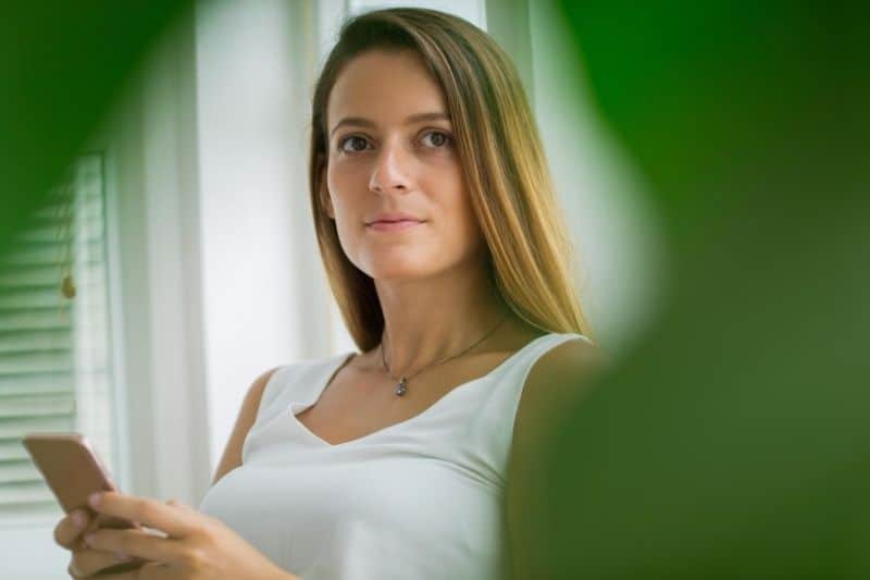 pensive attractive woman holding a smartphone with leave bordering her