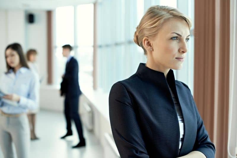 pensive businesswoman standing near the buildings glass wall with office people at the back