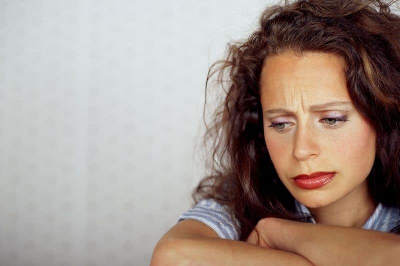 pensive woman bothered arms crossed sitting near white wall